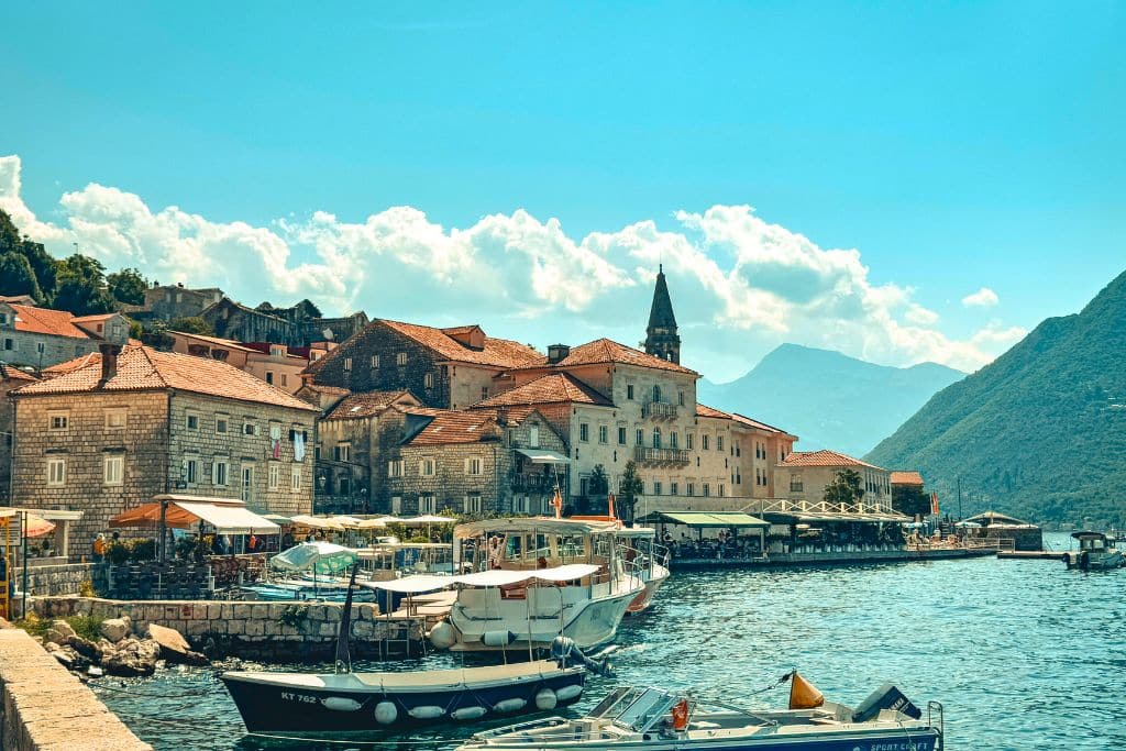 The picturesque waterfront village of Perast sits along the stunning Bay of Kotor, surrounded by mountains, stone buildings, and sparkling Adriatic waters.
