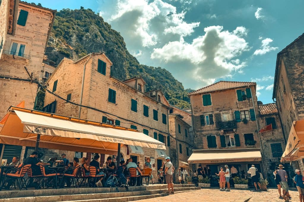 People enjoy outdoor cafes and wandering the charming cobblestone squares of Kotor Old Town beneath Montenegro’s dramatic mountain scenery.