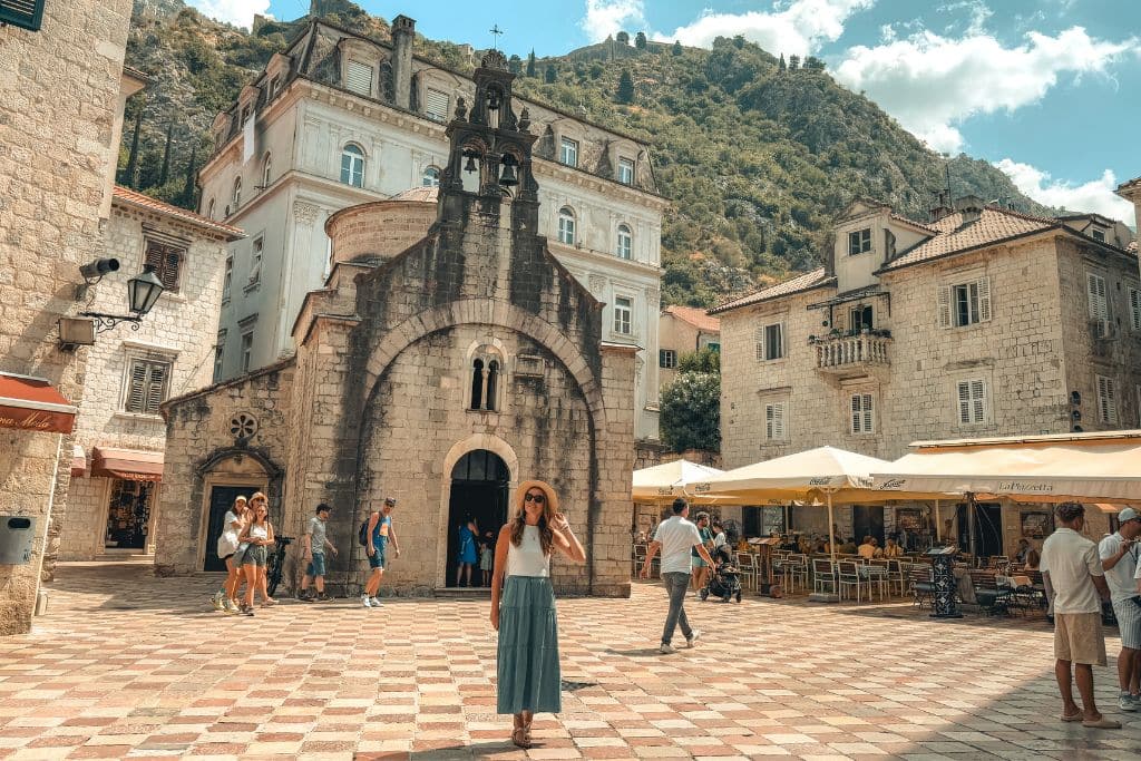 Kate walking through a courtyard in front of a church in the old town of Kotor Montenegro on a Day Trip.