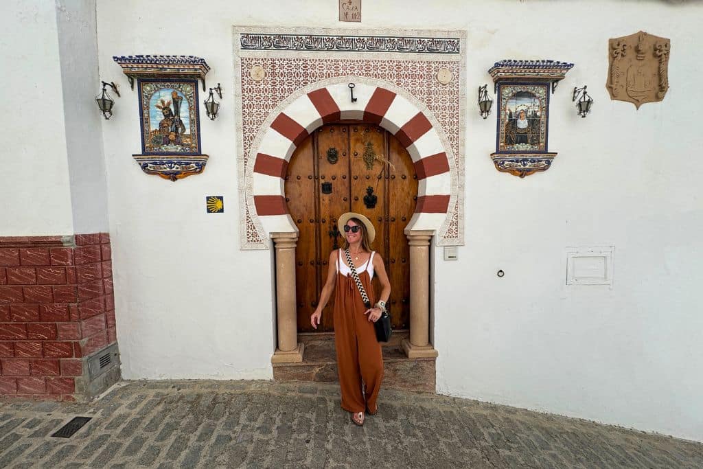 Kate explores a charming European street in summer, standing in front of a beautiful arched doorway with colorful Mediterranean tilework and historic architecture.