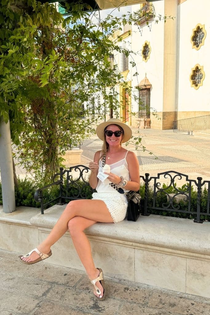 Kate wearing a lightweight white tank top, linen shorts, wide brim hat, and comfortable sandals while enjoying gelato in Europe during summer.