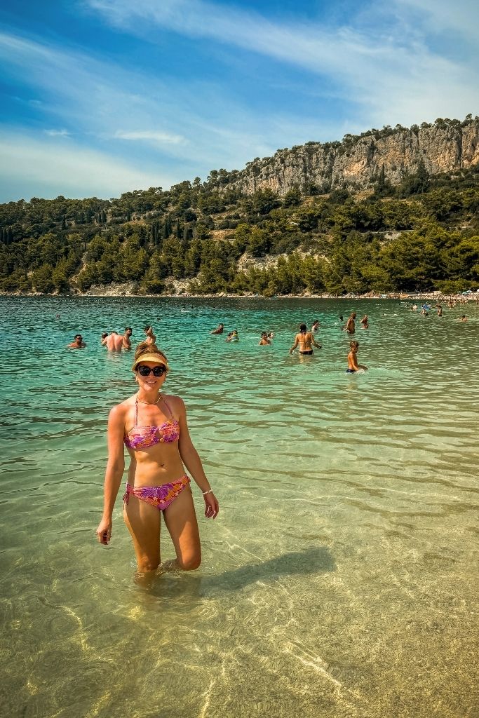 Kate wearing a colorful bikini, sunglasses, and a visor while swimming in the beautiful turquoise water along Europe’s stunning Mediterranean coastline in summer.