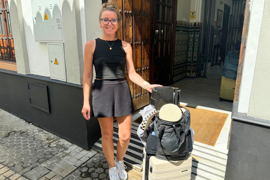 Kate wearing a simple black matching set, white sneakers, and a backpack while checking into her accommodation during a summer trip through Europe.