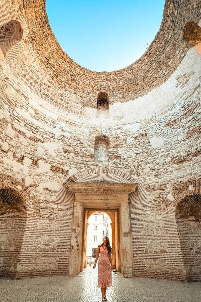 Kate walking beneath the ruins of Diocletian's Palace in Split, Croatia alone in a sundress as she looks up at them.