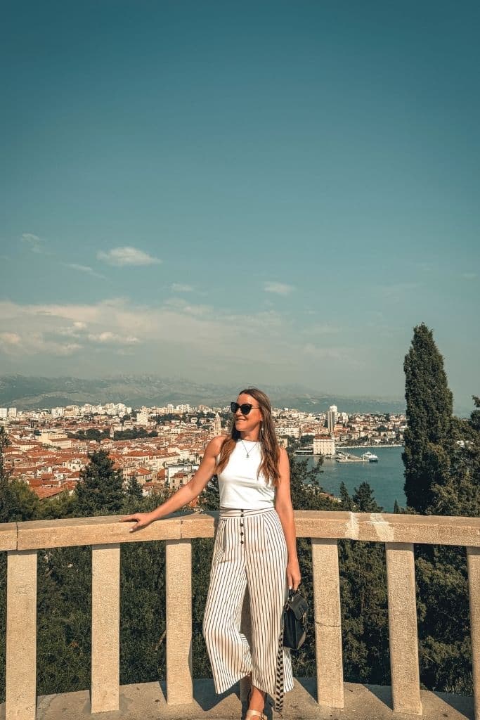 Kate stands on a terrace smiling with the view of Splits old town in the distance behind her.