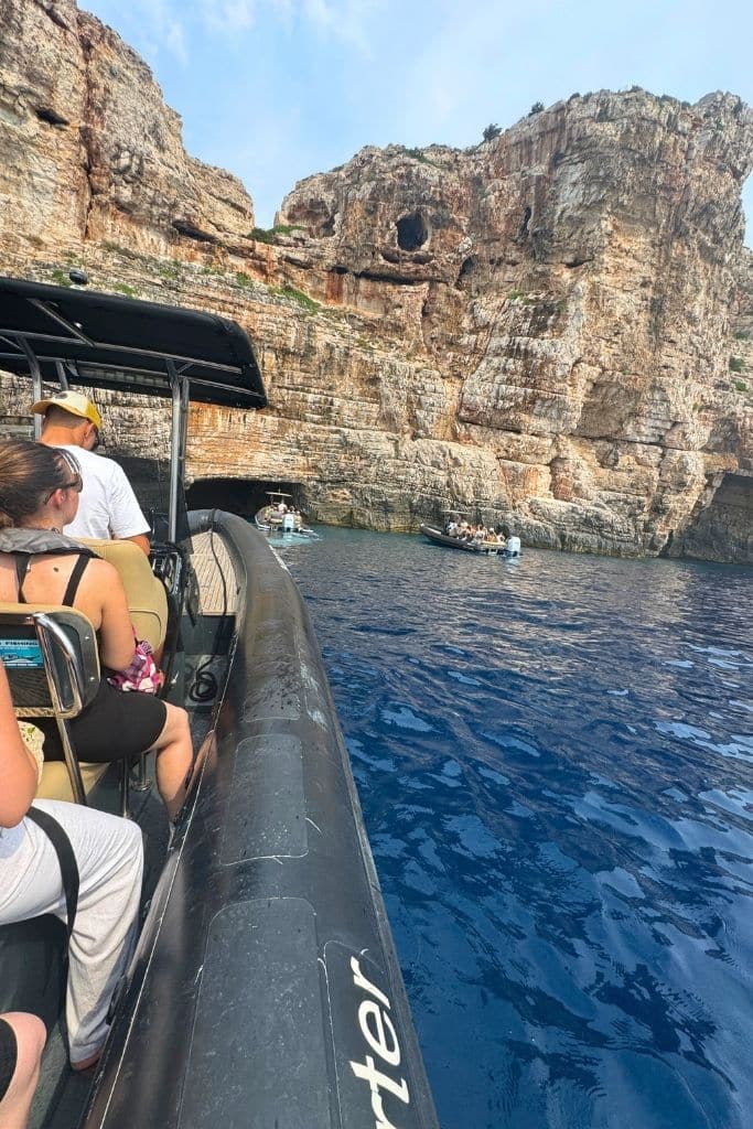People sitting in a raft boat with a rocky coastline in view, surrounded by deep blue water.