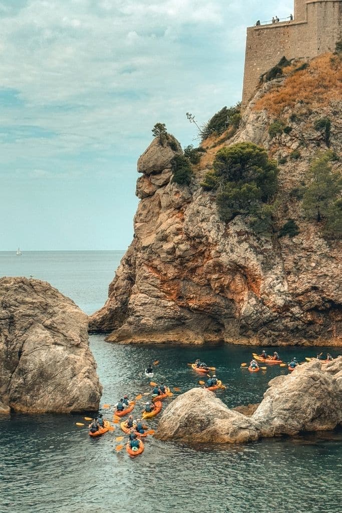 A group of kayakers kayaking between the rock croppings along the coastline of Dubrovnik.