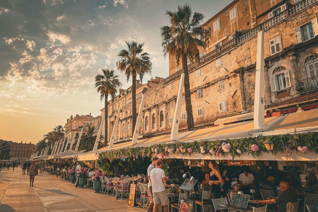Restaurants and palm trees line the waterfront in Split, Croatia at sunset.