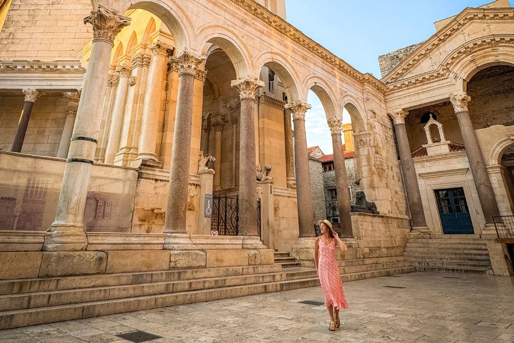 Kate walking through the main square of Diocletian's Palace in Split. She's wearing a pink sundress and sun hat and is smiling. 
