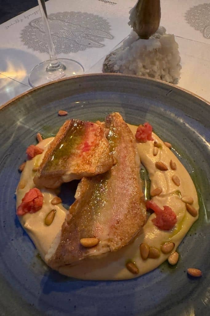 A plate with fresh catch of the day fish centered in a puree with pine nuts and flowers garnishing the plate.