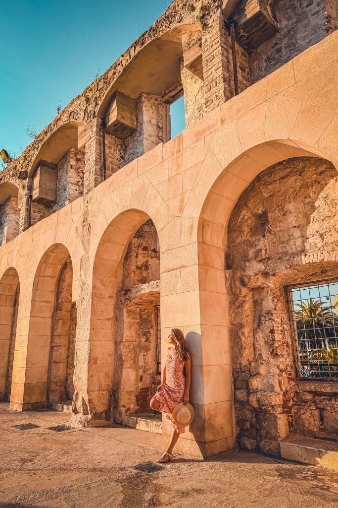 Kate leaning against a wall of arches in Split Croatia in the early golden light as the sunrises.