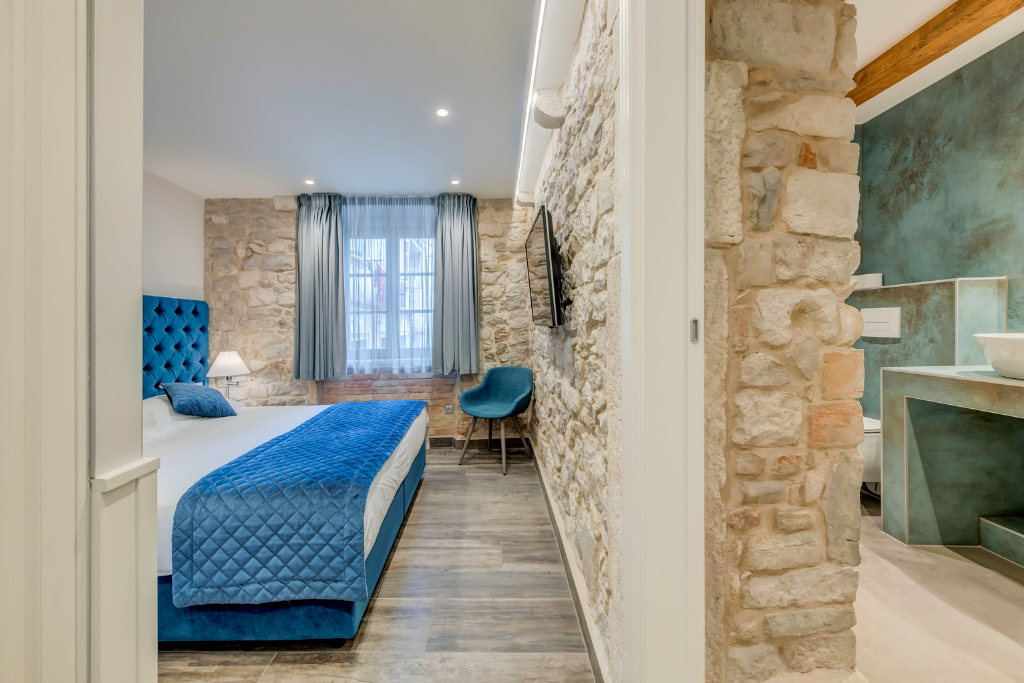 View of a hotel room with a natural stone wall dividing the bed and bathroom. 
