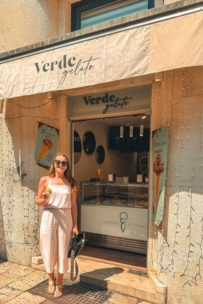Kate standing outside a gelato shop holding a scoop in a pink romper.