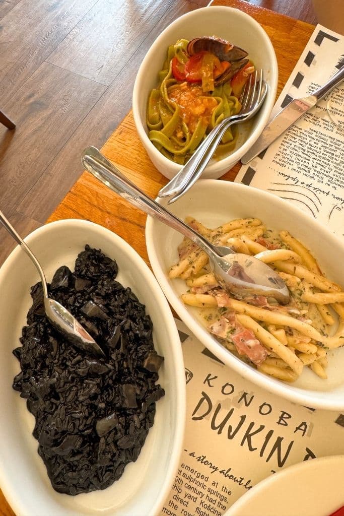 Three different dishes of risotto and seafood pasta set on a table.