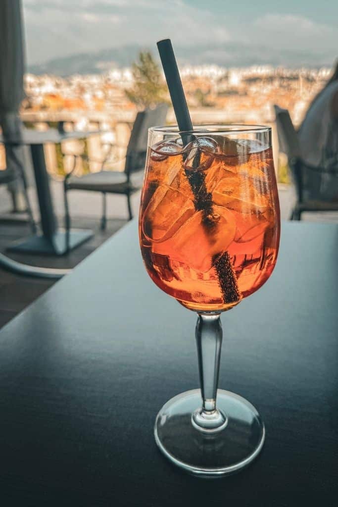 A tall glass of Apperol Spritz on a black table with a view of Croatia in the background.