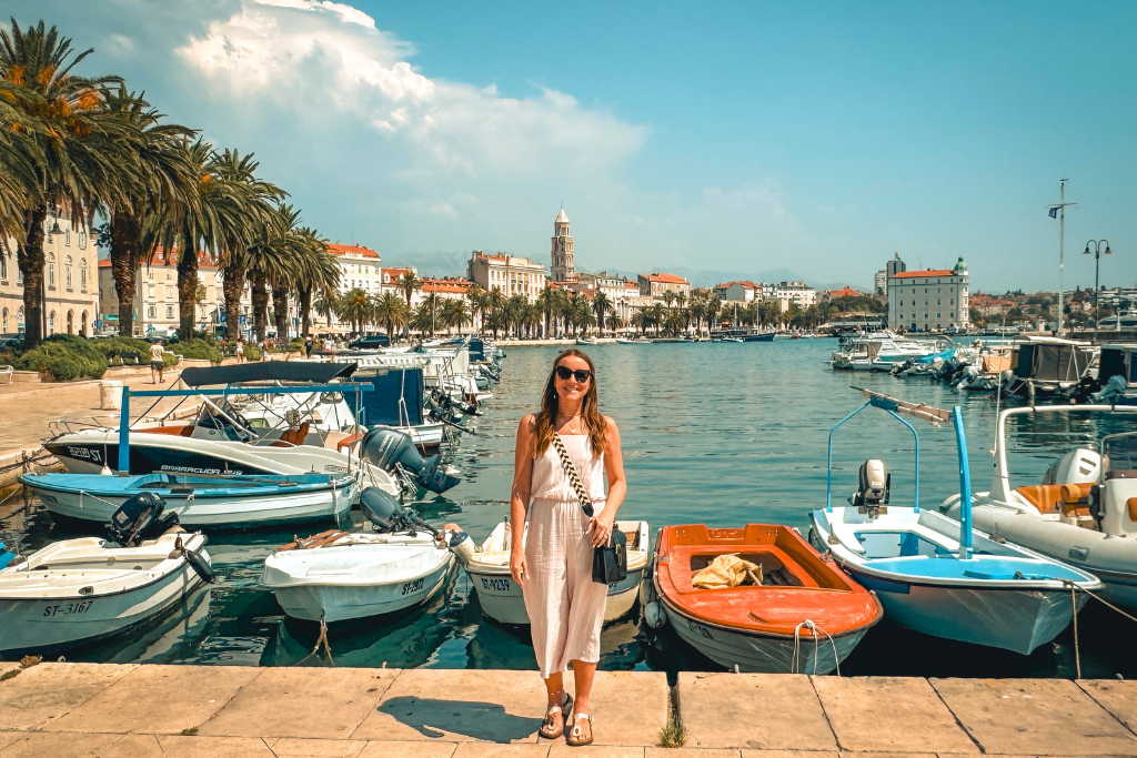 Kate standing next to the Marina in Split with boats and palm trees behind her on a sunny day in Split Croatia.