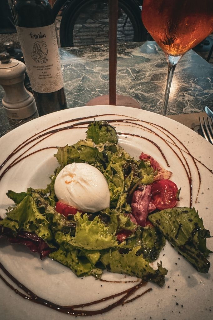 A fresh burrata salad with a big glob of burrata cheese, letuce and tomato, drizzled with dressing on a marble table in the evening.