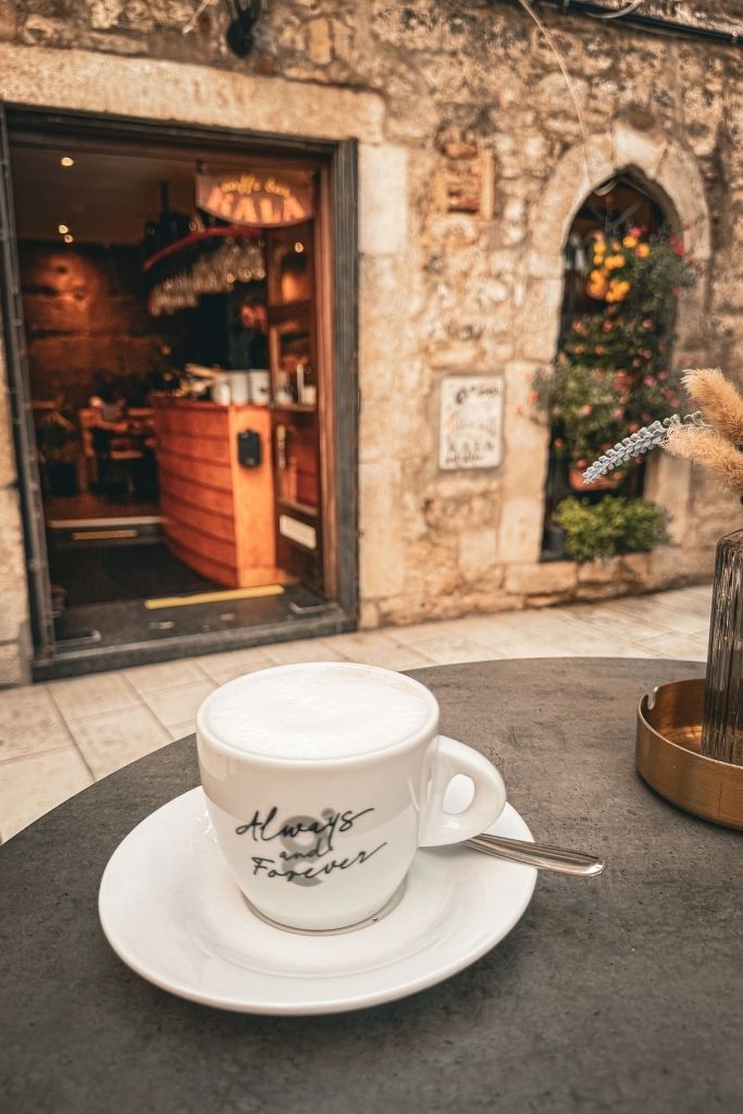 Cappuccino on a outside table in front of a cafe on a cobblestone street.