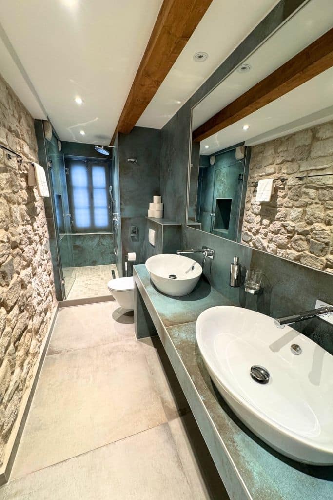 Bathroom with two sinks and large walk in shower with natural stone walls.
