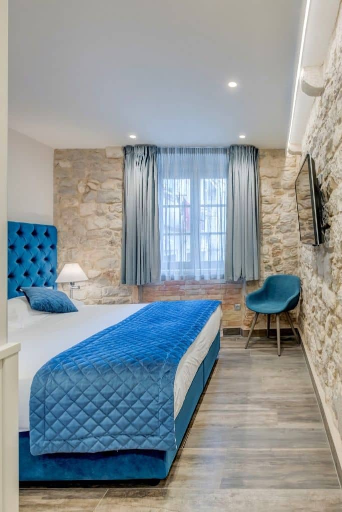 Natural sone walls and hardwood floors with a large bed in a bright room at Mint Luxury Rooms in Split