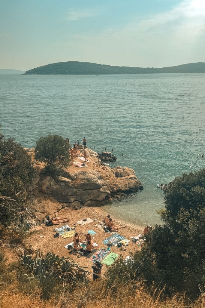 A small hidden beach tucked in between rocks where people are swimming, lounging and jumping. 