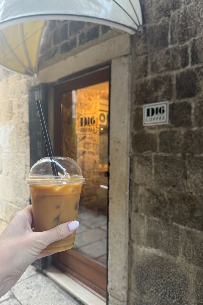Kate's hand holding up a to go coffee with the D16 coffee shop in the background.