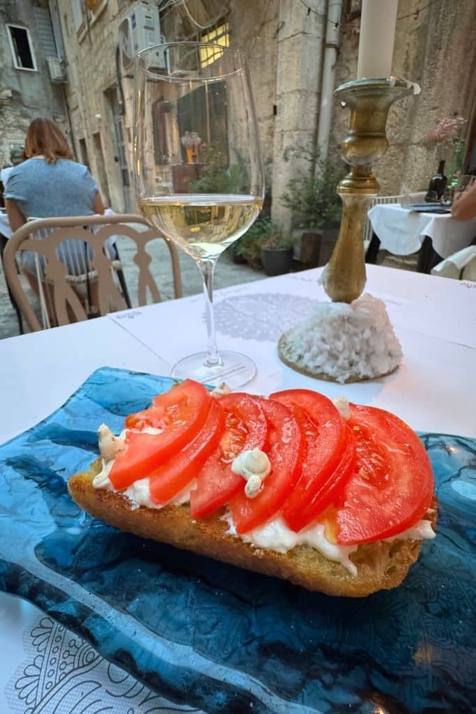 A blue plate with fresh bruschetta and a glass of white wine on a white table cloth