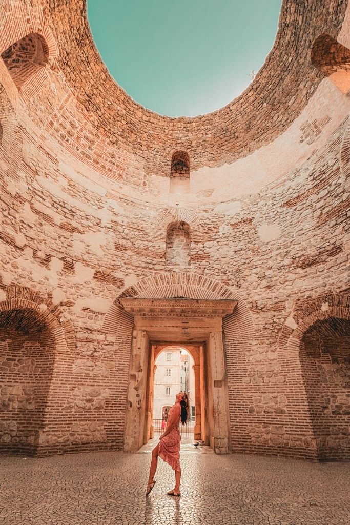 Kate stands inside the ancient Vestibule of Diocletian's Palace, looking up at the open circular ceiling surrounded by towering Roman stone walls.