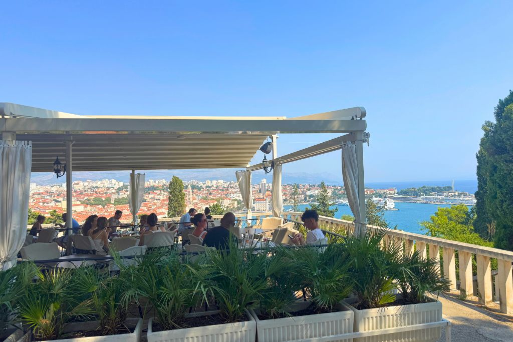 A terrace café on Marjan Hill overlooks Split's Old Town and harbor, where visitors relax with drinks while enjoying panoramic views of the city and Adriatic Sea.