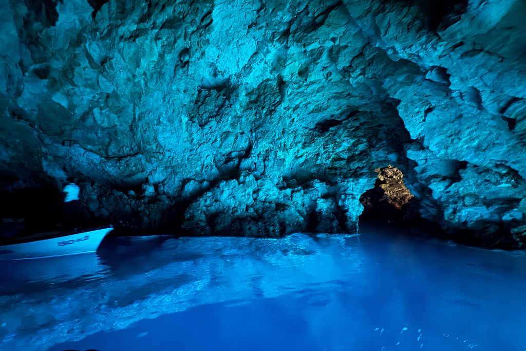 The Blue Cave glows with an otherworldly blue light as sunlight reflects through the water, illuminating the cave's rocky walls and creating a vivid blue shimmer across the surface.