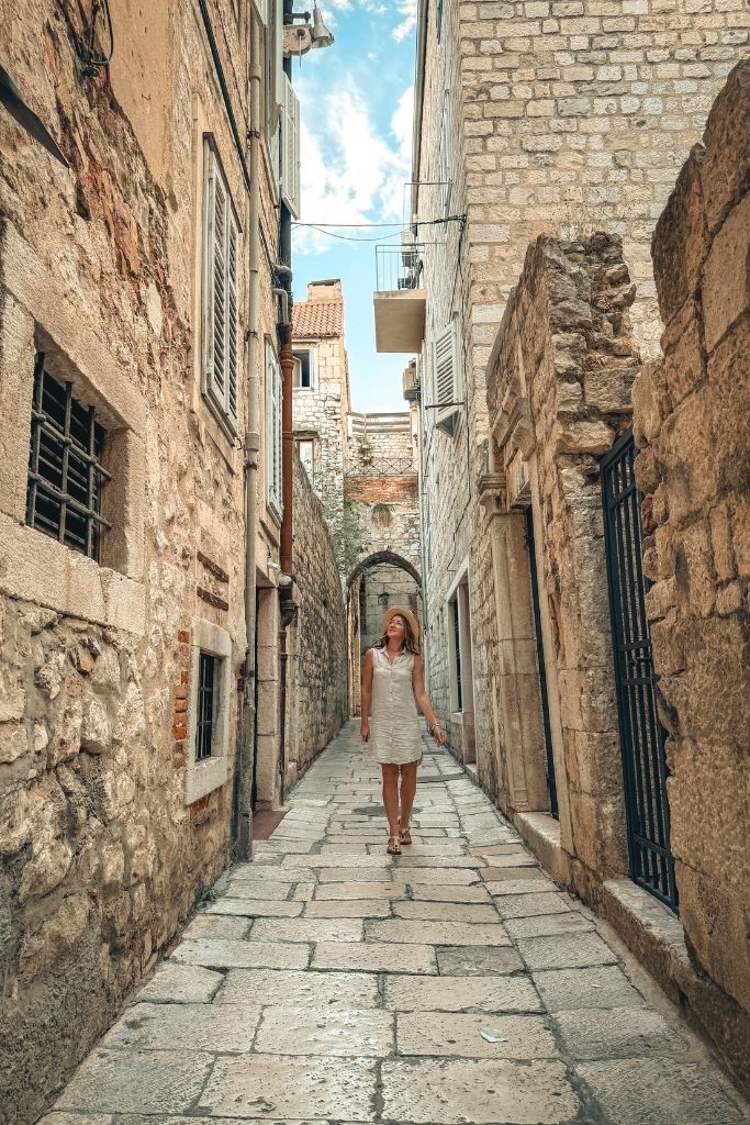 Kate walks through a narrow stone alleyway in Split's Old Town, surrounded by centuries-old buildings that showcase the city's historic charm and hidden corners.