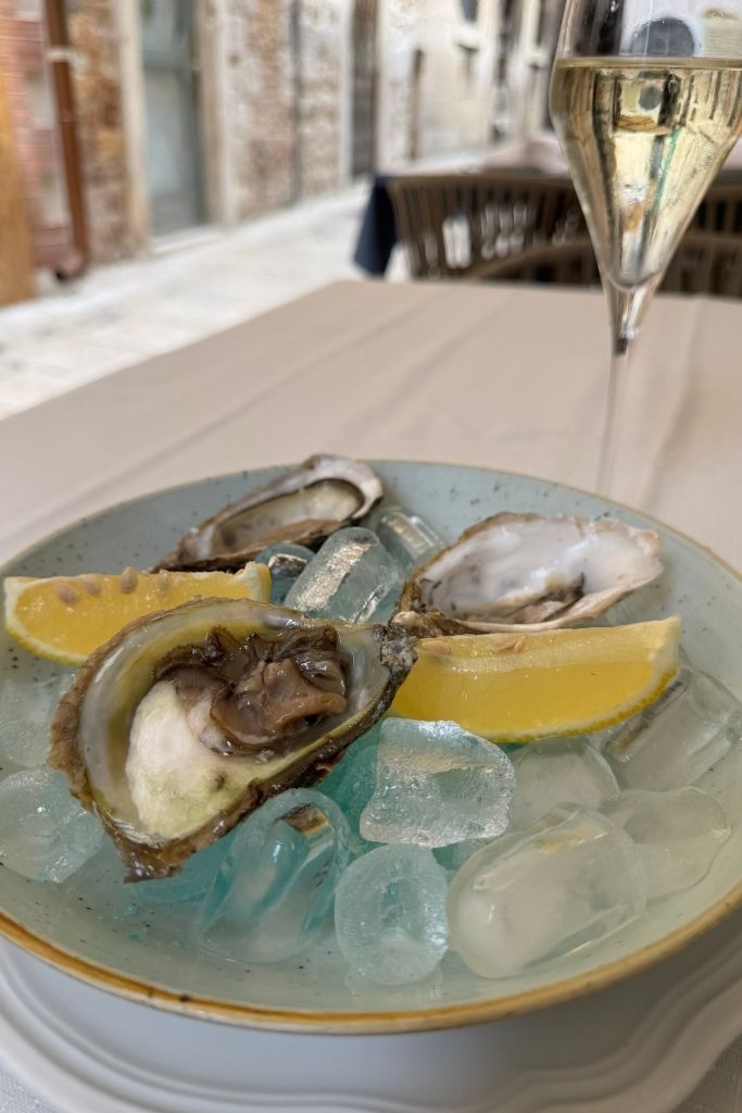 Fresh oysters served on ice with lemon wedges are paired with a glass of sparkling wine, showcasing one of the best local seafood delicacies to try during a visit to Split.