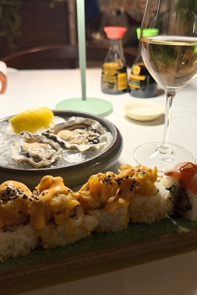 A plate of sushi rolls and fresh oysters is paired with a glass of white wine, creating an elegant seafood dining experience in Split's Old Town.
