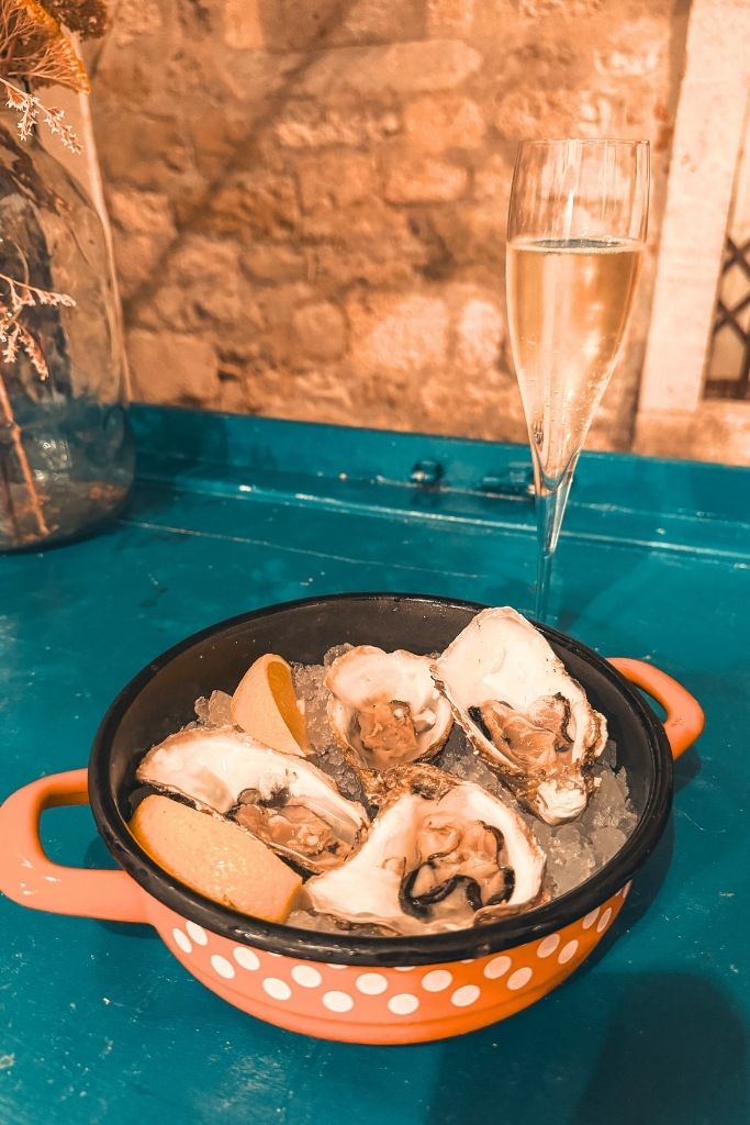 A plate of freshly shucked oysters served over ice with lemon wedges sits beside a glass of sparkling wine, highlighting one of the most memorable seafood experiences near Split.
