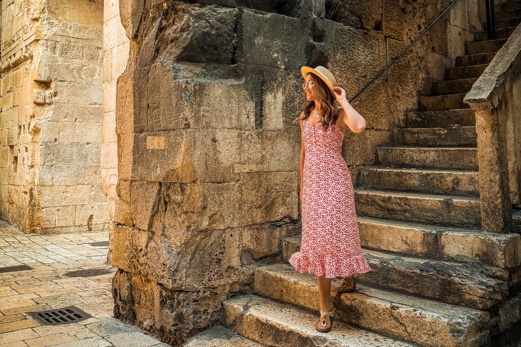 Kate walks down a worn stone staircase tucked within Diocletian's Palace, surrounded by massive Roman walls that showcase the ancient history woven throughout Split's Old Town.