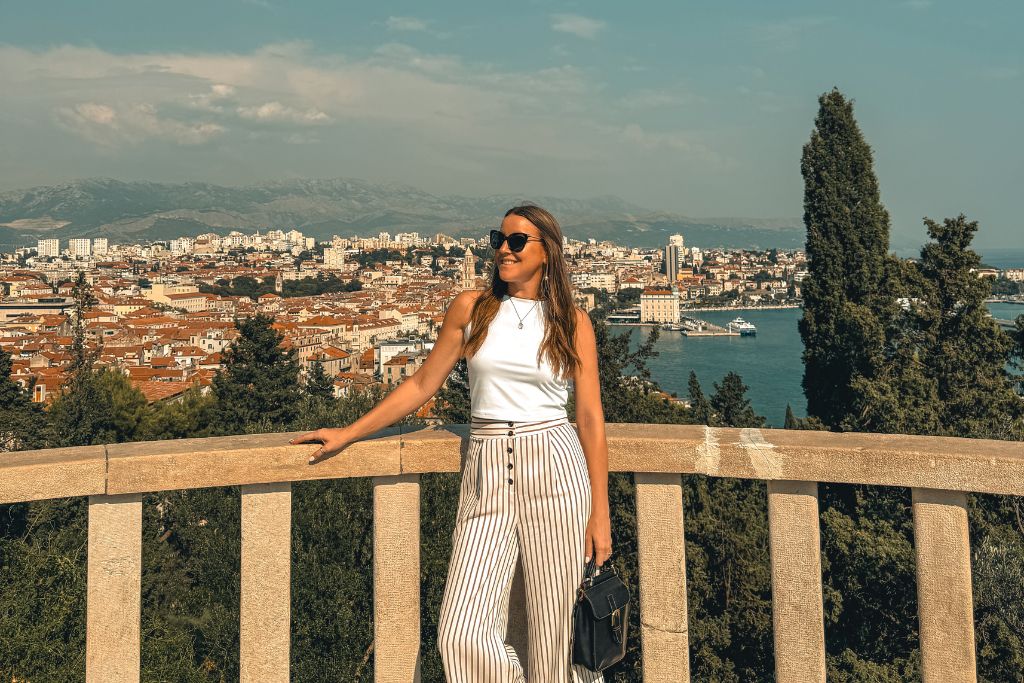 Kate stands at a scenic overlook on Marjan Hill, with sweeping views of Split's red rooftops, harbor, and mountains stretching across the horizon behind her.