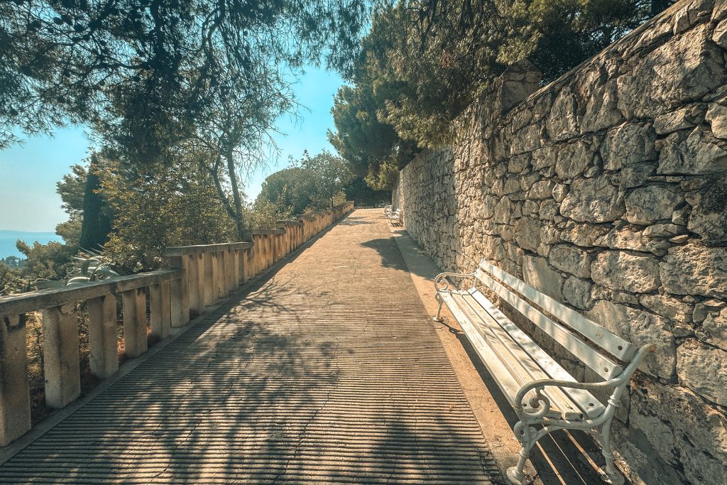 A shaded walking path winds through Marjan Hill, with stone walls, benches, and pine trees creating a peaceful place to rest during the climb to the viewpoints above Split.