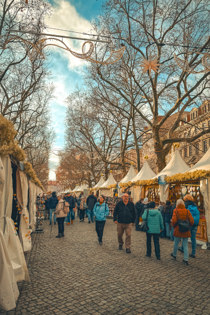 Strolling through one of Dresden’s festive Christmas markets, where rows of decorated stalls, twinkling lights, and star-shaped ornaments create a cozy holiday atmosphere.