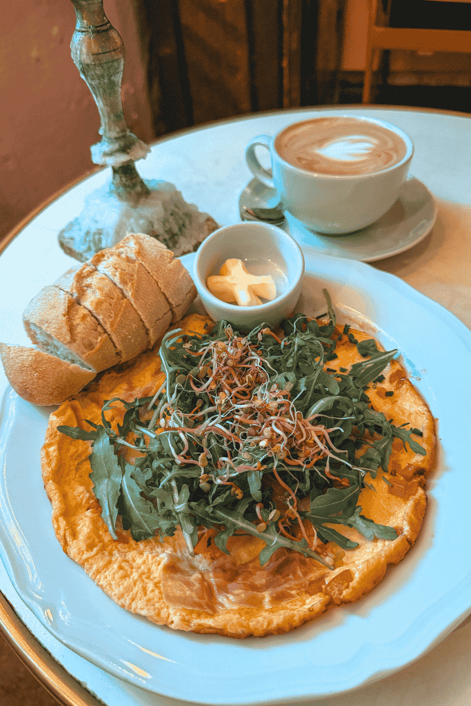 A fresh omelet topped with arugula and sprouts, served with bread and a cappuccino at Café Camelot in Krakow.