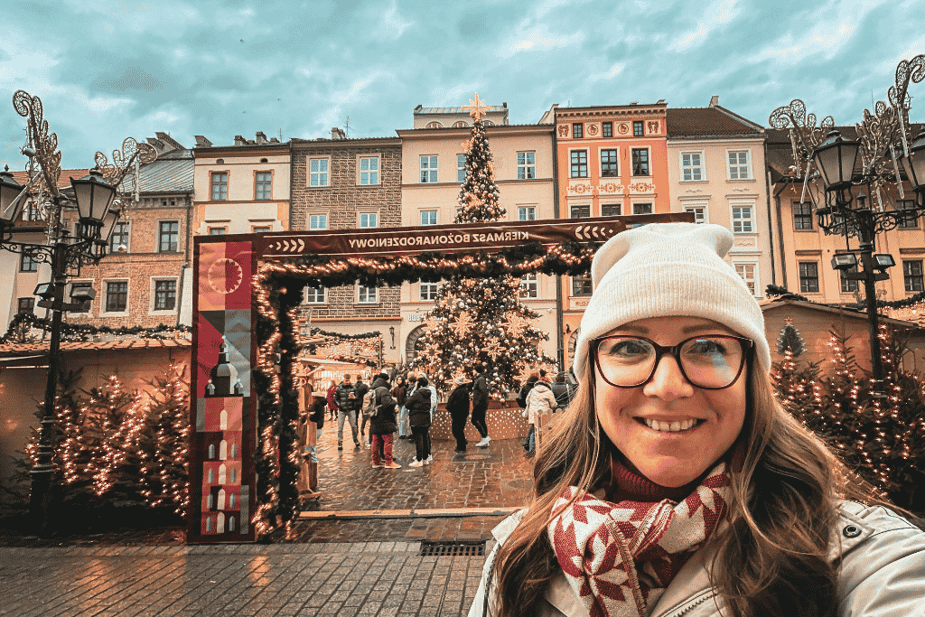 A selfie at the Little Market Square Christmas Market in Krakow, surrounded by festive Christmas trees, lights, and colorful historic buildings.