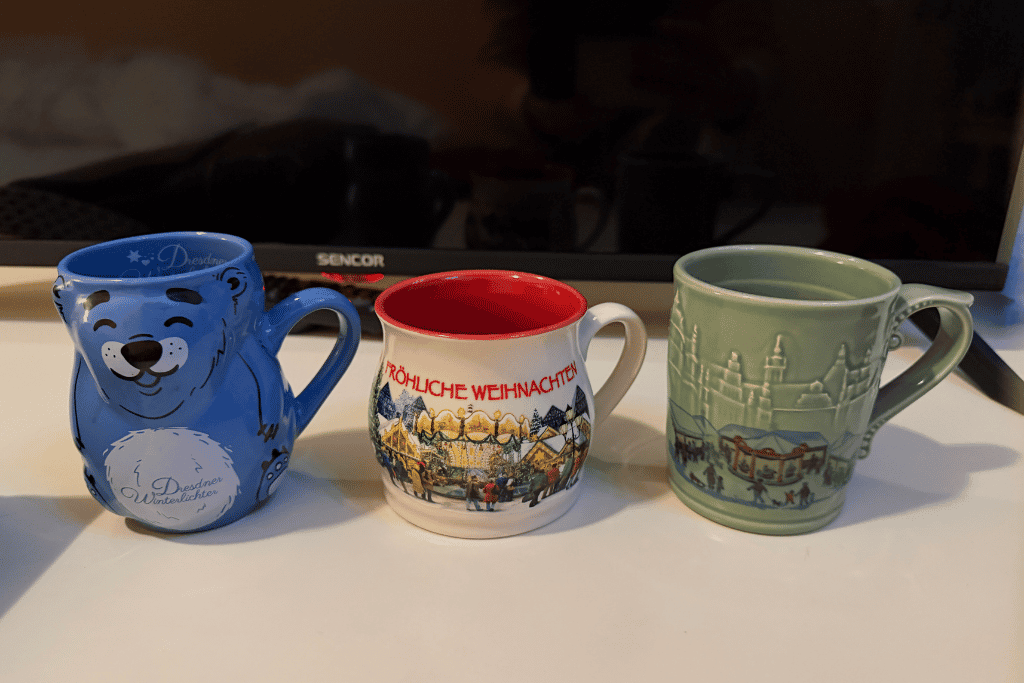 Dresden’s Striezelmarkt comes alive at twilight, when the Christmas tree, Ferris wheel, and rows of festive market stalls glow against the deep blue winter sky.

My growing collection of Dresden Christmas market mugs—one of my favorite souvenirs from sipping Glühwein while exploring the city’s festive markets.