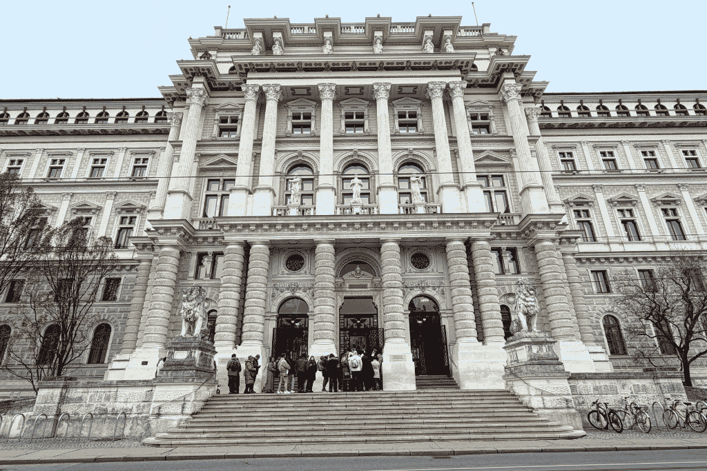The grand front entrance of Vienna’s Palace of Justice features tall columns, stone statues, wide steps, and people gathered outside.