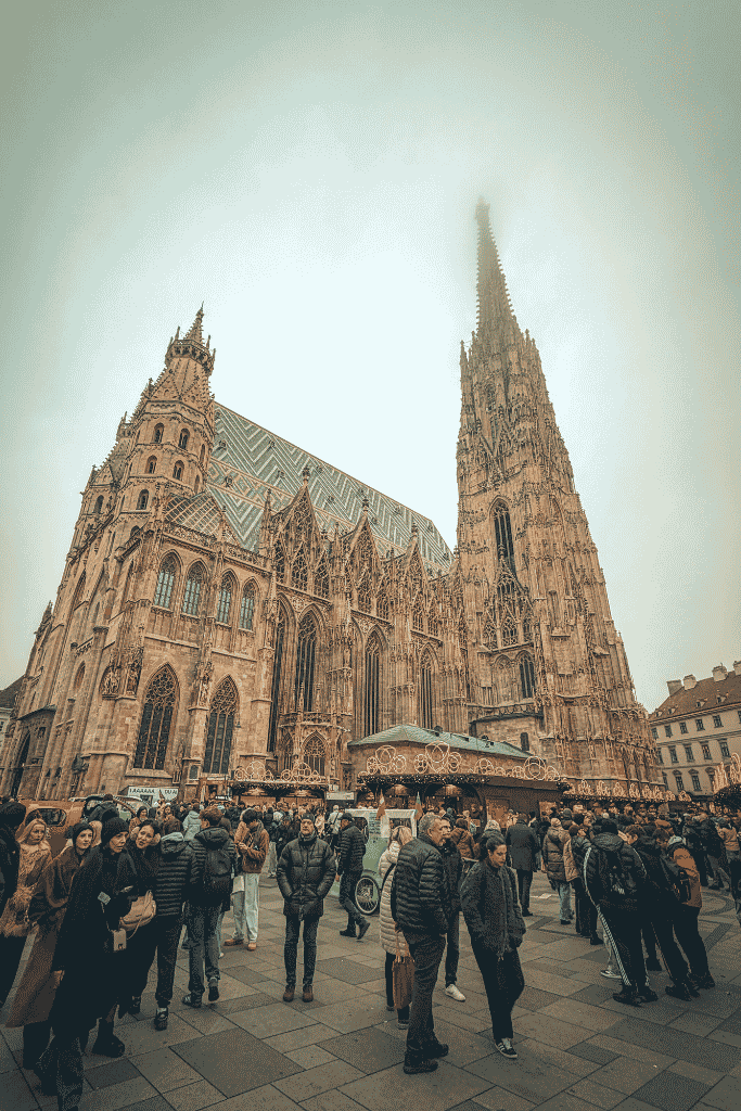 St. Stephen’s Cathedral rises above a crowded Christmas market in central Vienna on a cloudy winter day.