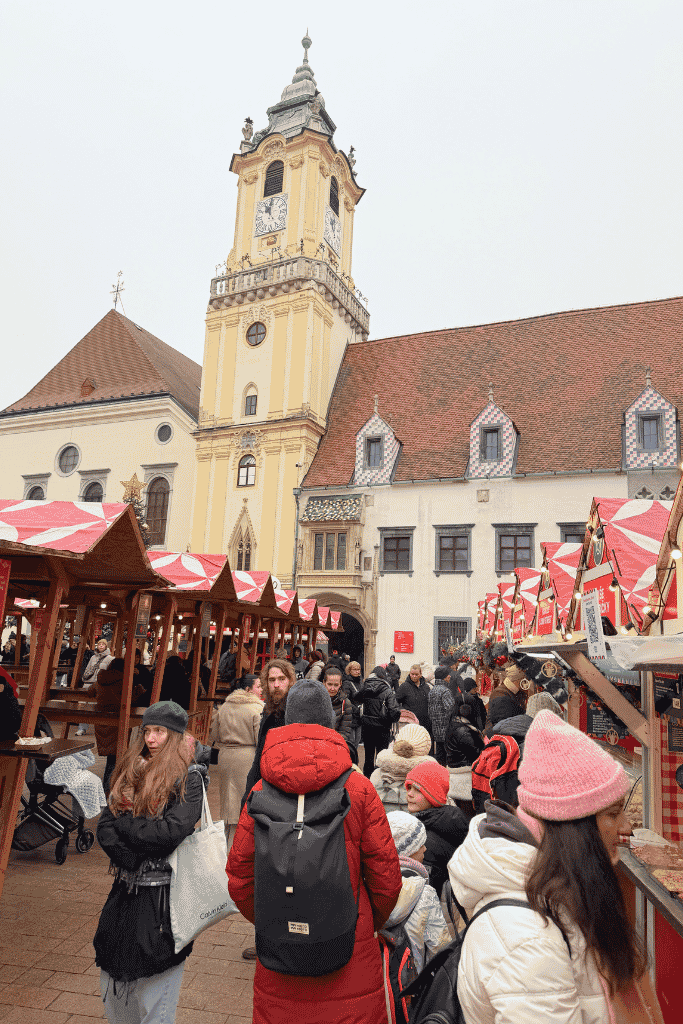 A busy Christmas market fills the square in front of the Old Town Hall and its tall clock tower in Bratislava.