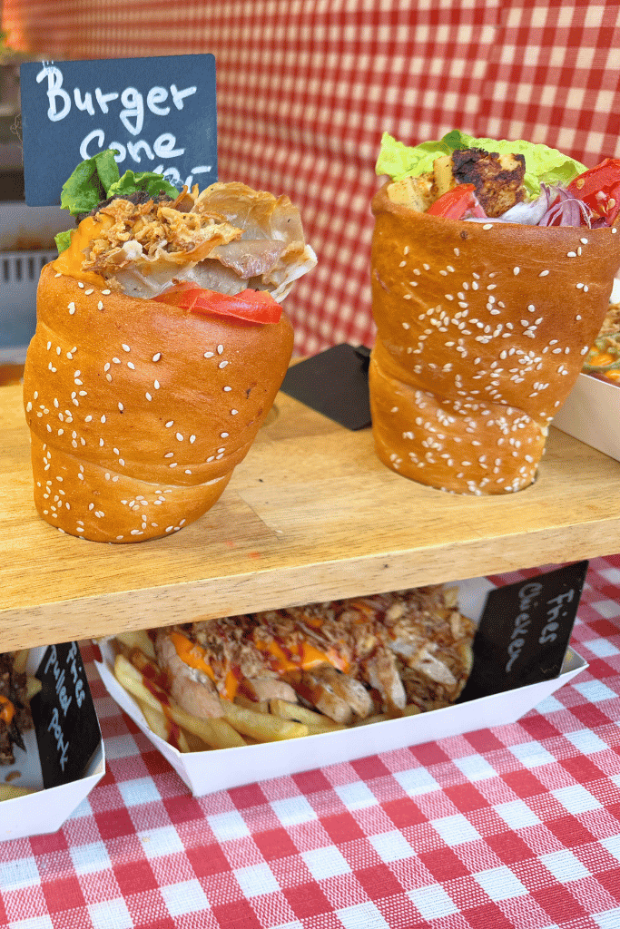 Two large sesame bread cones filled with meat, lettuce, tomatoes, onions, and sauce are displayed at a Christmas market food stall.