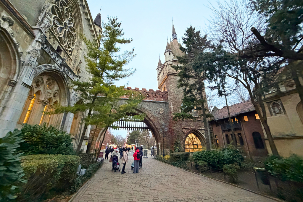 A stone archway and towers at Vajdahunyad Castle in Budapest, with visitors walking along the path.