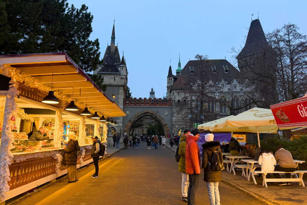 Christmas market stalls glow with warm lights in front of Vajdahunyad Castle in Budapest.