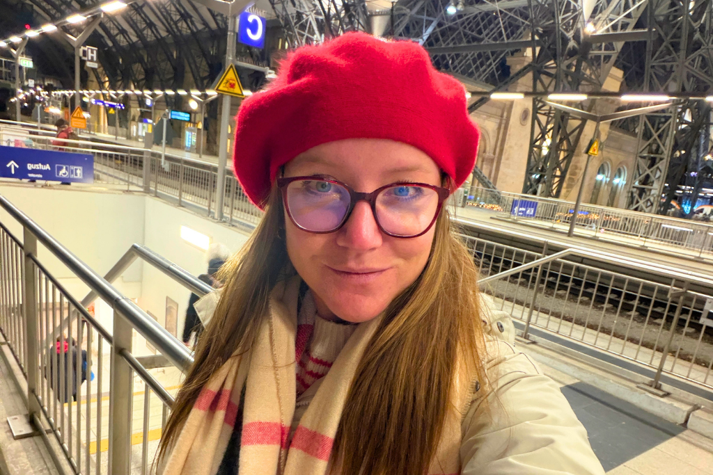 Kate in a red hat and glasses takes a selfie inside a train station.