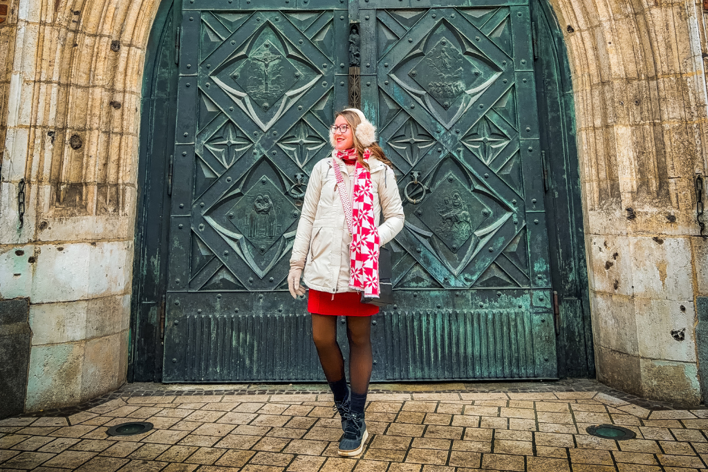 Kate in winter clothing posing in front of an ornate historic green door in Prague.