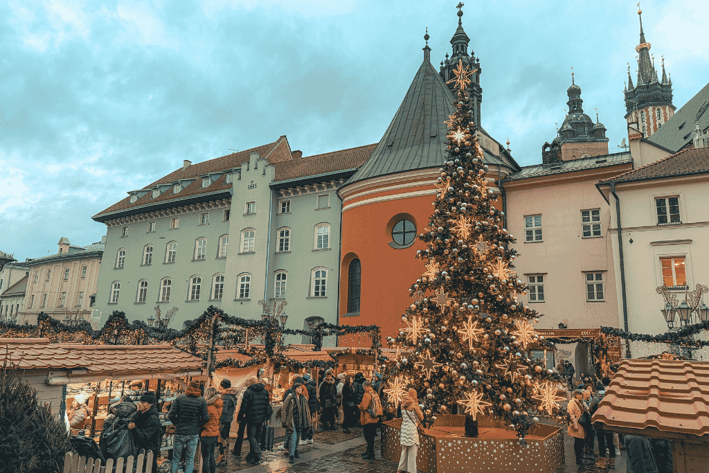 A large decorated Christmas tree surrounded by festive market stalls in Little Market Square in Krakow, Poland.